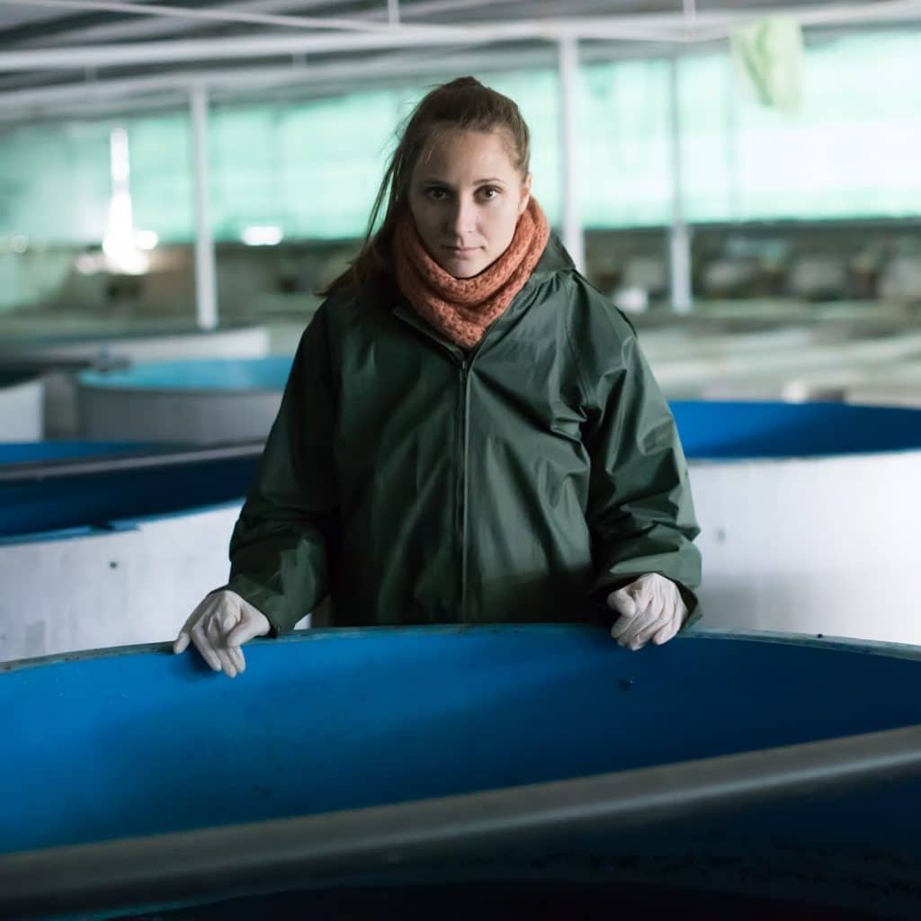 Young woman owner of sturgeon farm watching fish in pool